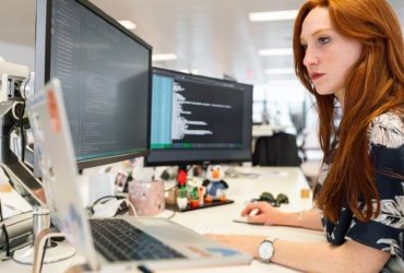 redhead woman working on multiple computer screens at office