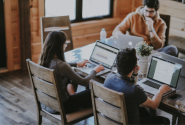 Three people sitting at large table working on their laptops.