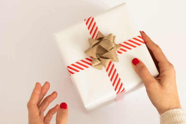 Woman resting hand on gift with white wrapping paper, red and white striped ribbon, and bow.