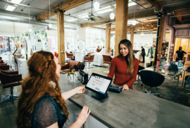 A female small business owner behind desk at salon with a female customer paying for service on the other side of the desk