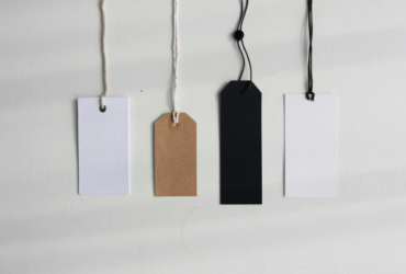 A row of clothing tags next to each other varying in size, shape, and colour.