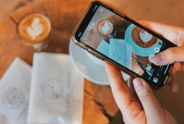 Person holding mobile phone and taking a photo of a business's coffee and logo