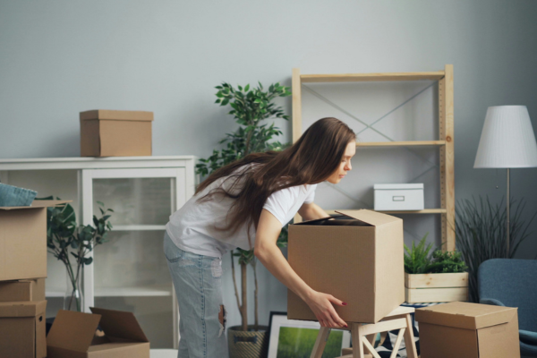 A woman picking up a cardboard box inside home.