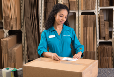 Woman looking down at large cardboard box while placing a shipping label on it.