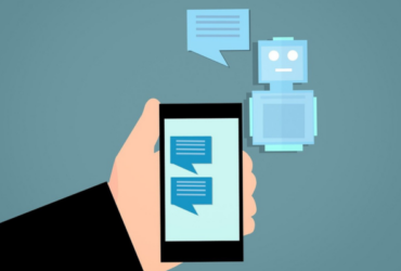 Illustration of hand holding a mobile phone with chat bubbles on the screen, and a robot and chat bubble floating in the air