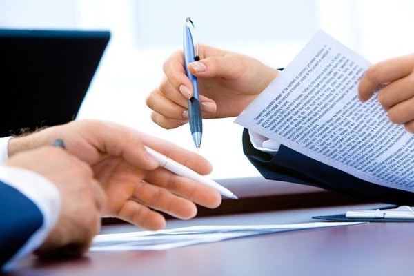 Two people's hands holding documents and pens