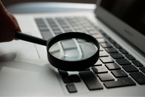 person holding magnified glass on laptop keyboard