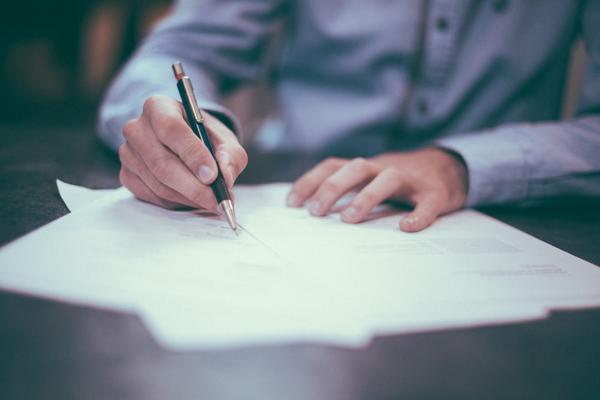 person signing papers with pen on table