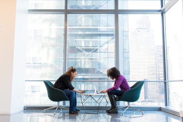 Two people sitting on chairs at small table in front of floor-to-ceiling glass windows