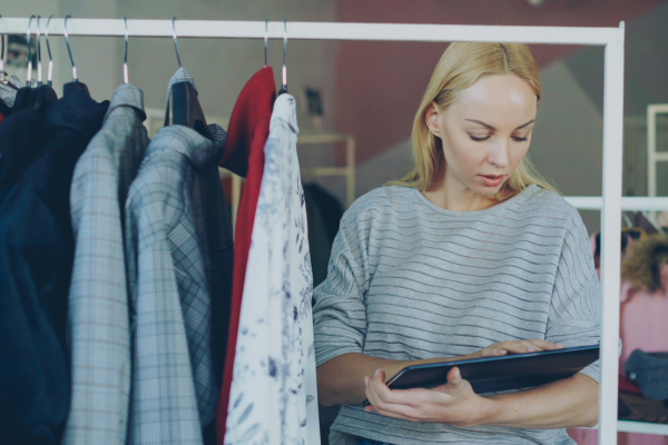 A woman looking at tablet beside a clothing rack