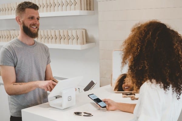 A man behind the counter at a store and a woman paying with her phone