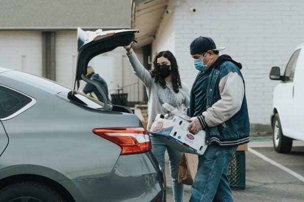 Image of an employee wearing a mask and putting a box in a woman's car