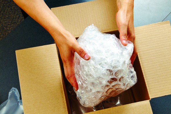 hands putting a bubble wrapped item in a box