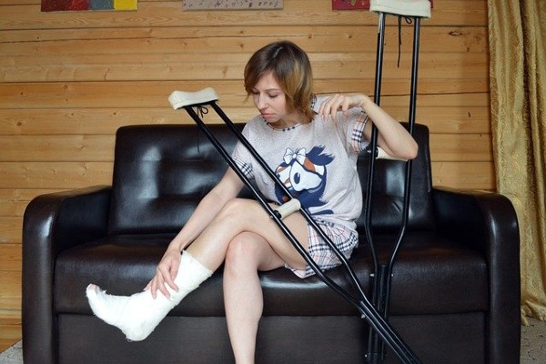 A blond woman sitting on a couch with crutches and her foot in a cast