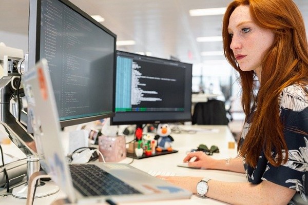 redhead woman working on multiple computer screens at office