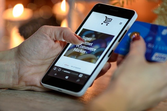 A woman's hands holding a credit card and a phone while online shopping