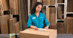 Woman looking down at large cardboard box while placing a shipping label on it.