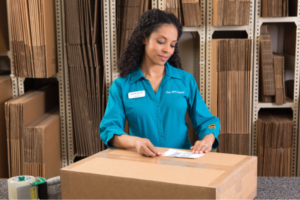 Woman looking down at large cardboard box while placing a shipping label on it.