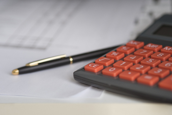 A calculator with red number keys on a small stack of paper beside a pen