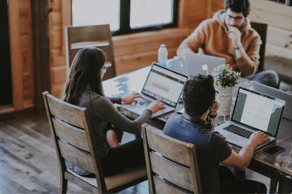 Three people sitting at large table working on their laptops.