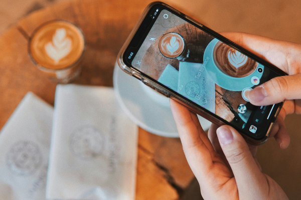 Person holding mobile phone and taking a photo of a business's coffee and logo